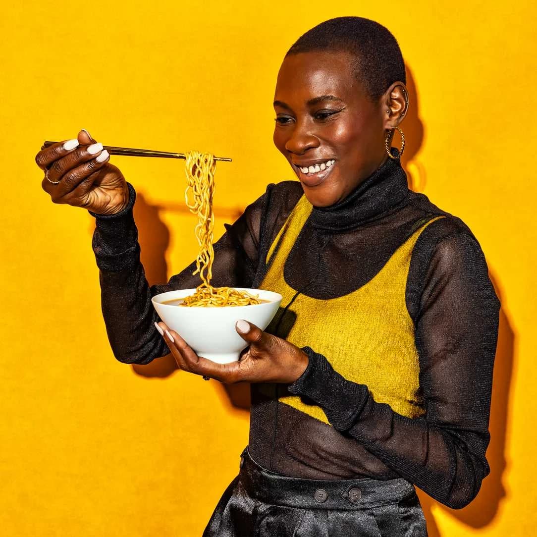 Woman smiling while eating Maruchan gold ramen in a bowl with chopsticks