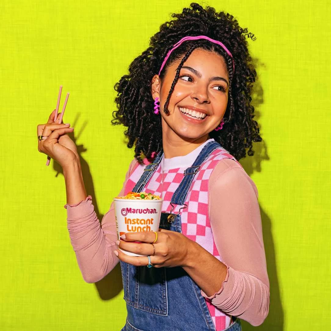Woman smiling while holding a cup of Maruchan instant lunch noodles and chopsticks