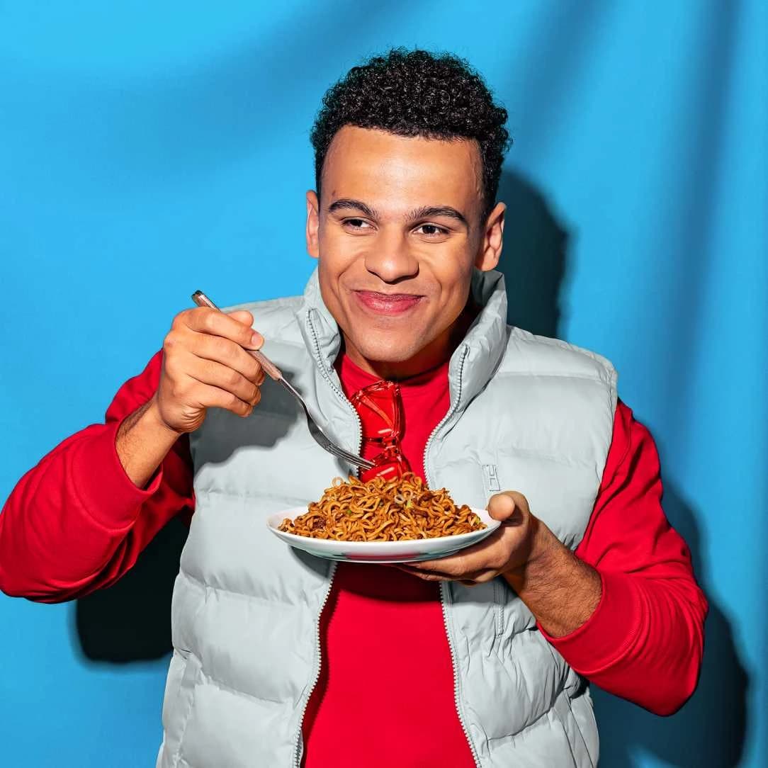 Man smiling while eating a plate of Korean BBQ Yakisoba noodles with a fork