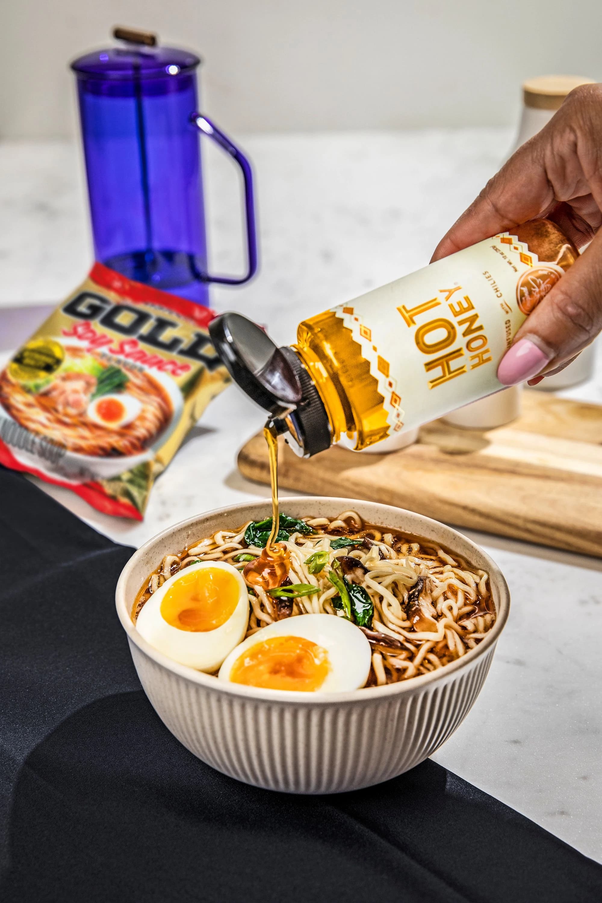 A bowl of gold soy sauce flavor ramen with eggs being drizzle with hot honey.