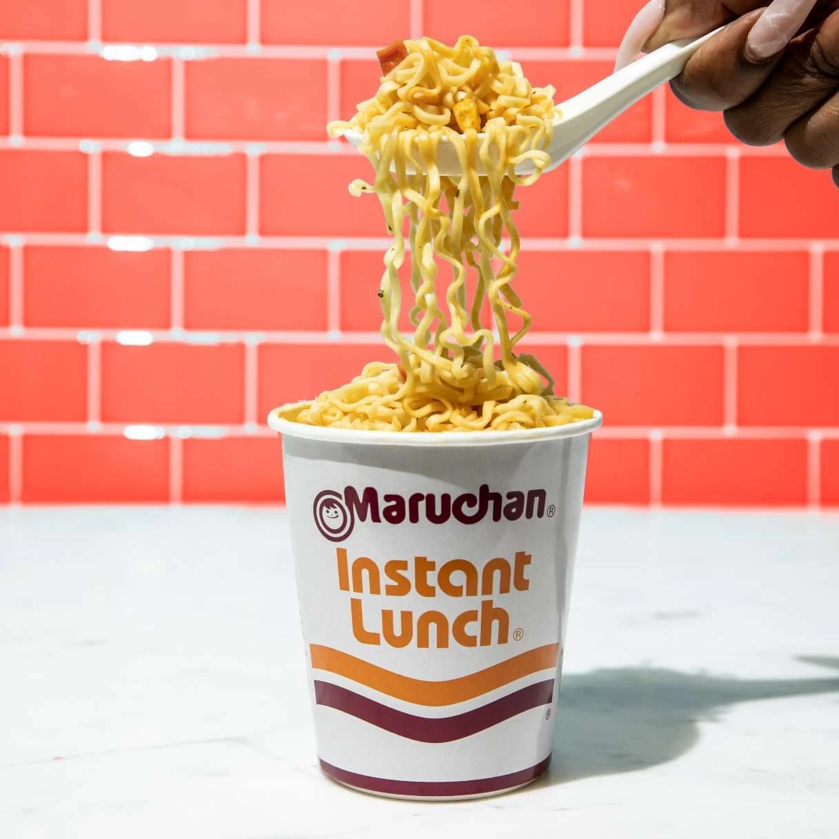 Instant lunch beef flavor ramen cup with noodles being scooped up while a spoon