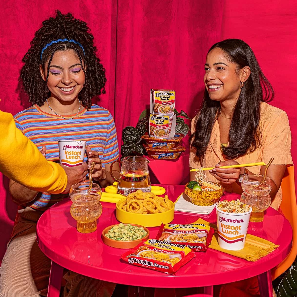 People smiling at a dining table with ramen foods on it