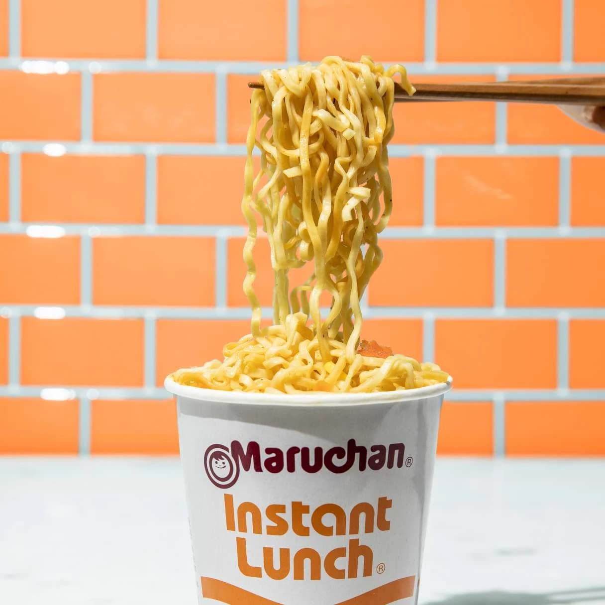 Cup of instant lunch chicken flavor ramen with chopsticks picking up noodles