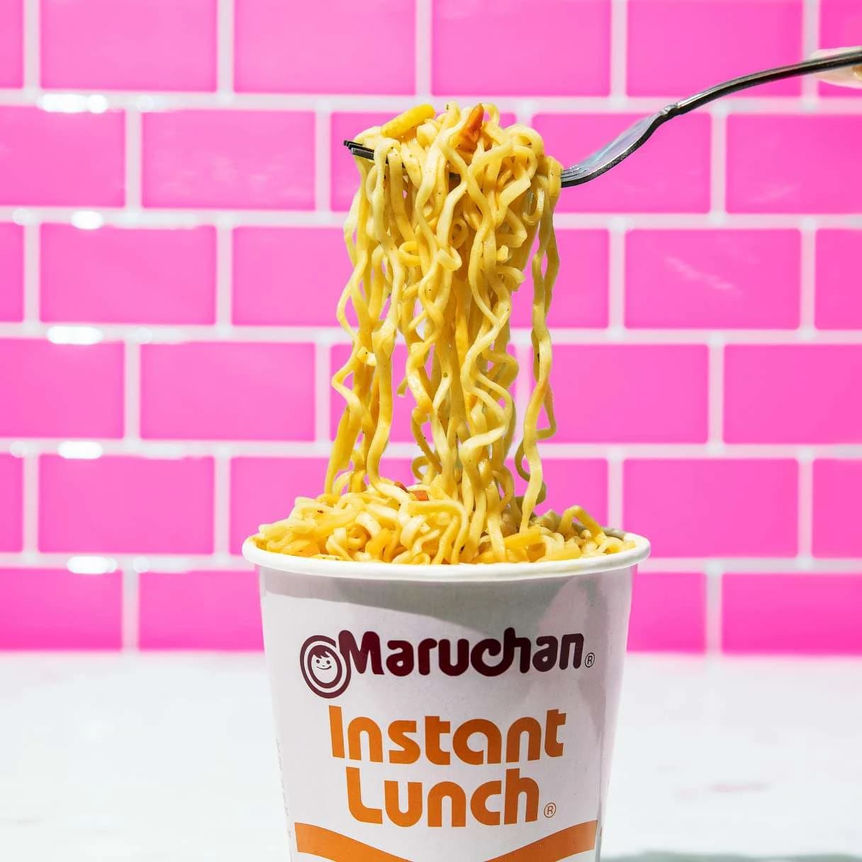 Cup of instant lunch hot and spicy shrimp flavor ramen with noodles being picked up with a fork