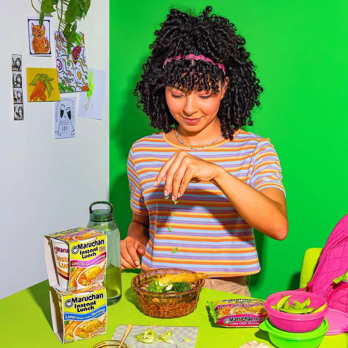 Woman eating a bowl of ramen with maruchan instant lunch packages on the table