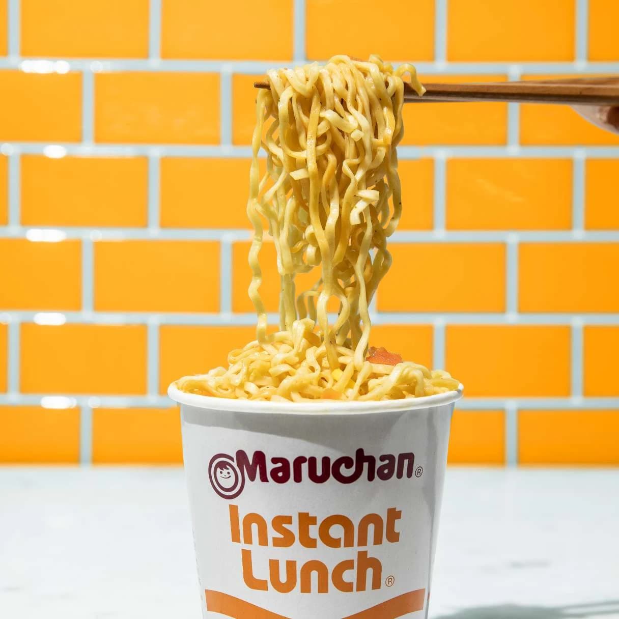 Cup of instant lunch select chicken flavor ramen with noodles being grabbed by chopsticks