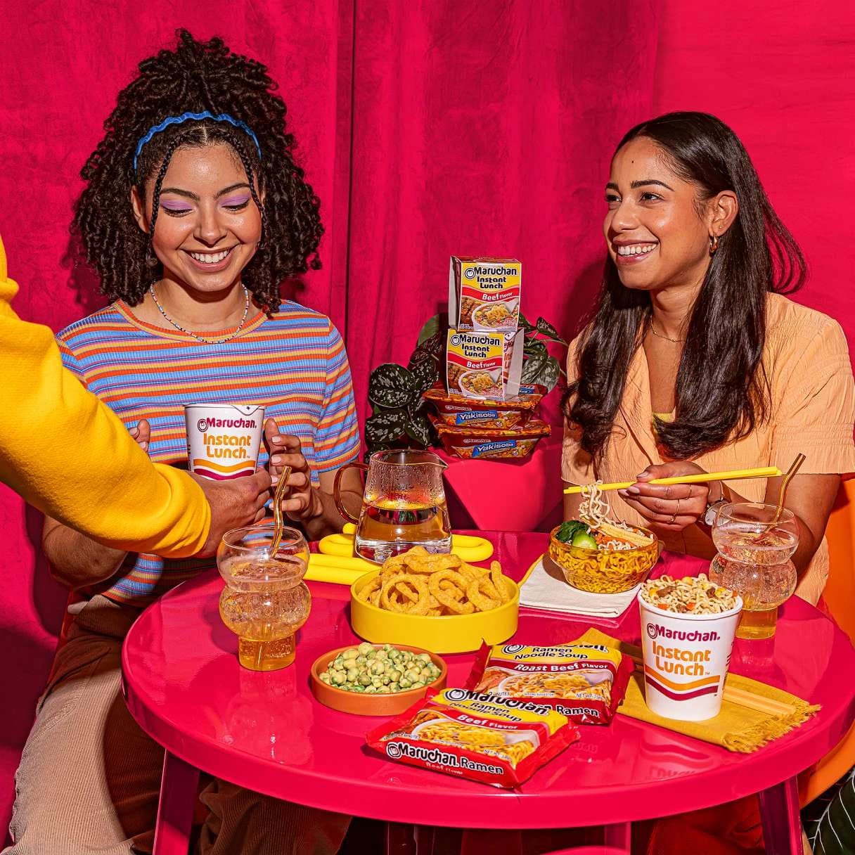 People sitting at a dining table, smiling and eating Maruchan ramen