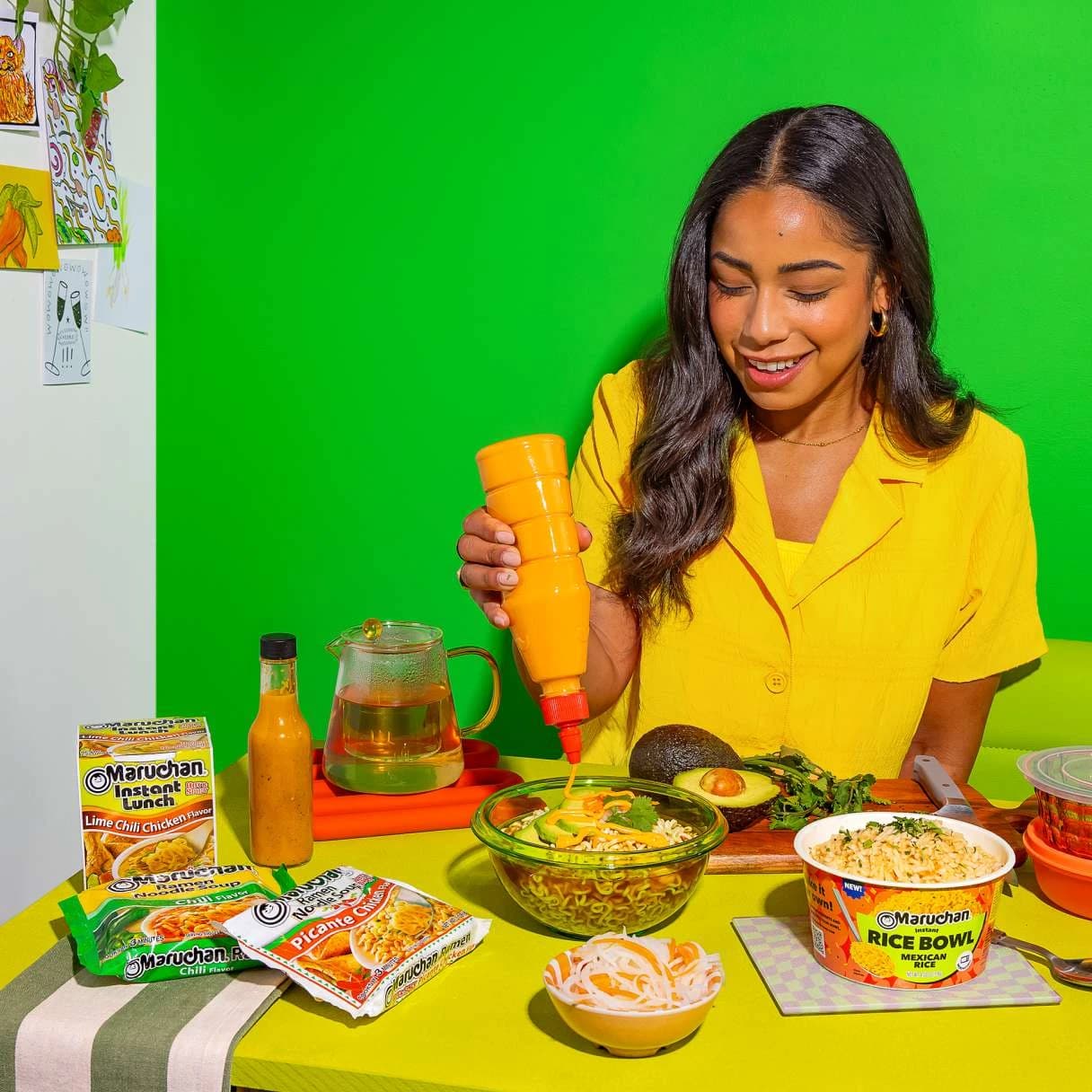 Woman squeezing sauce into bowl of ramen on a dining table with ramen packages