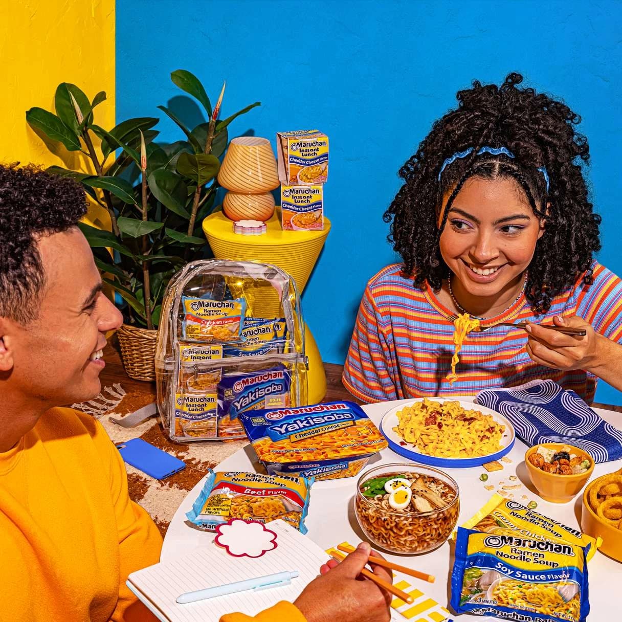 People sitting at a table, smiling, and eating a bowl of ramen
