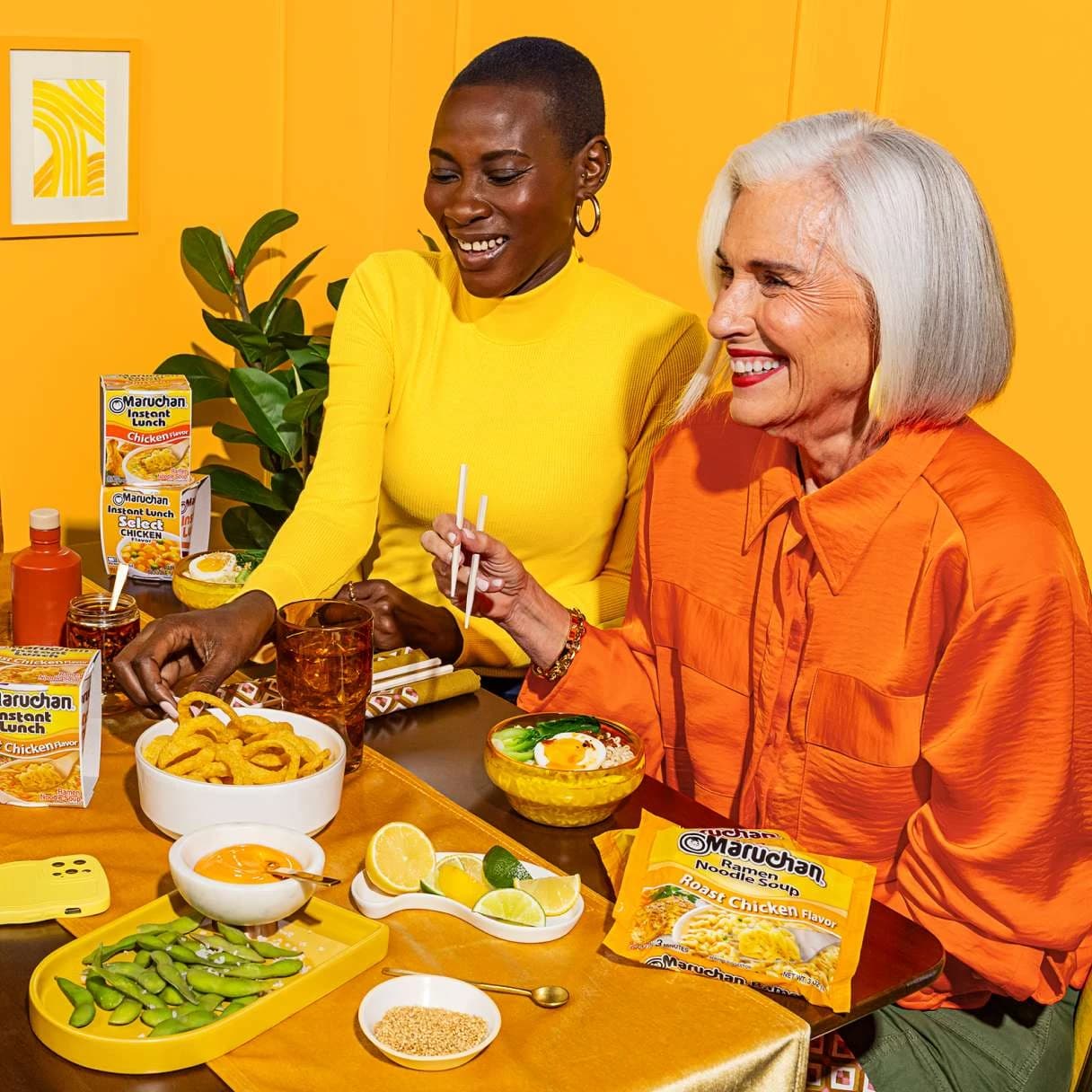 Women sitting at a dining table and smiling while eating Maruchan ramen