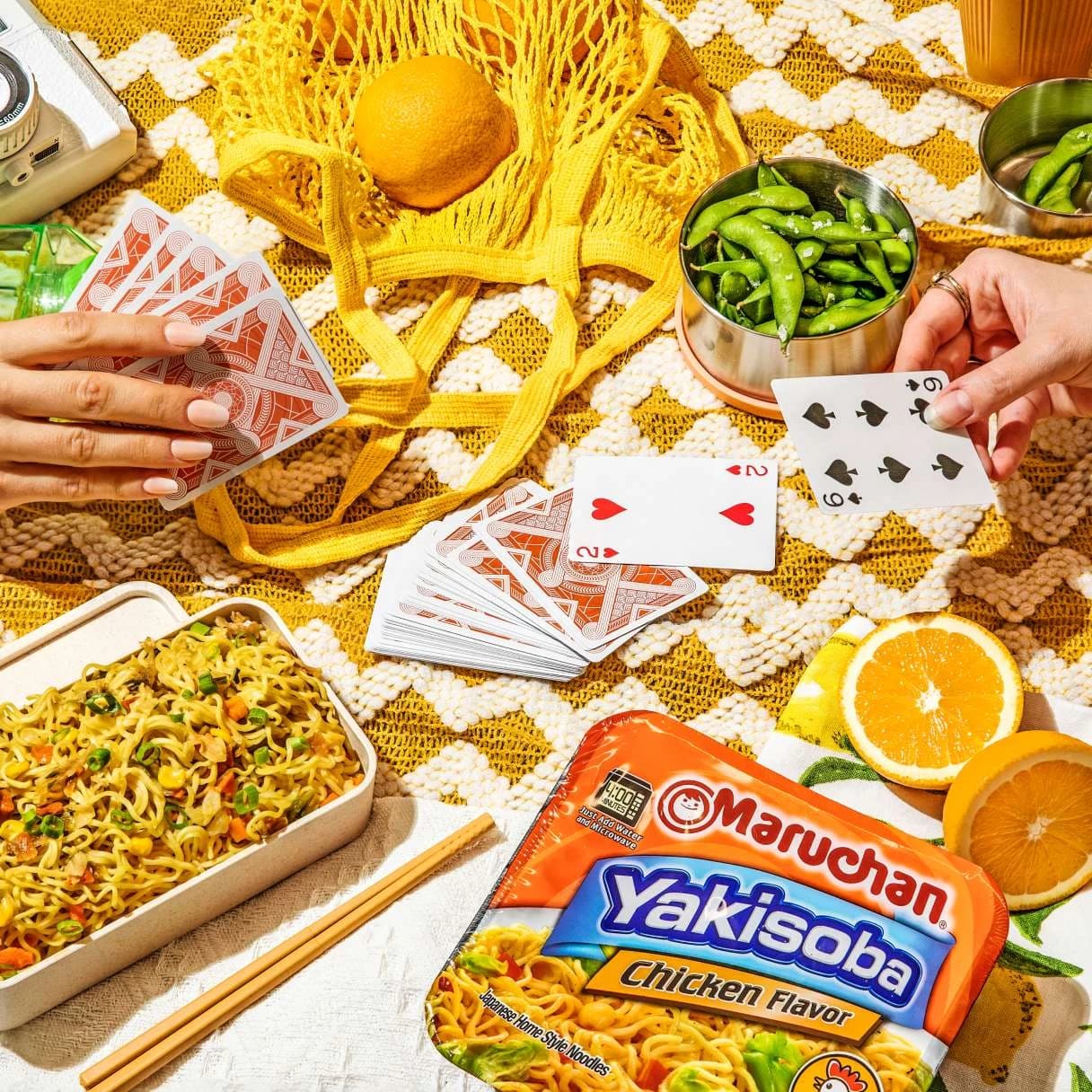 Chicken flavor yakisoba package on a table with food and people playing a card game