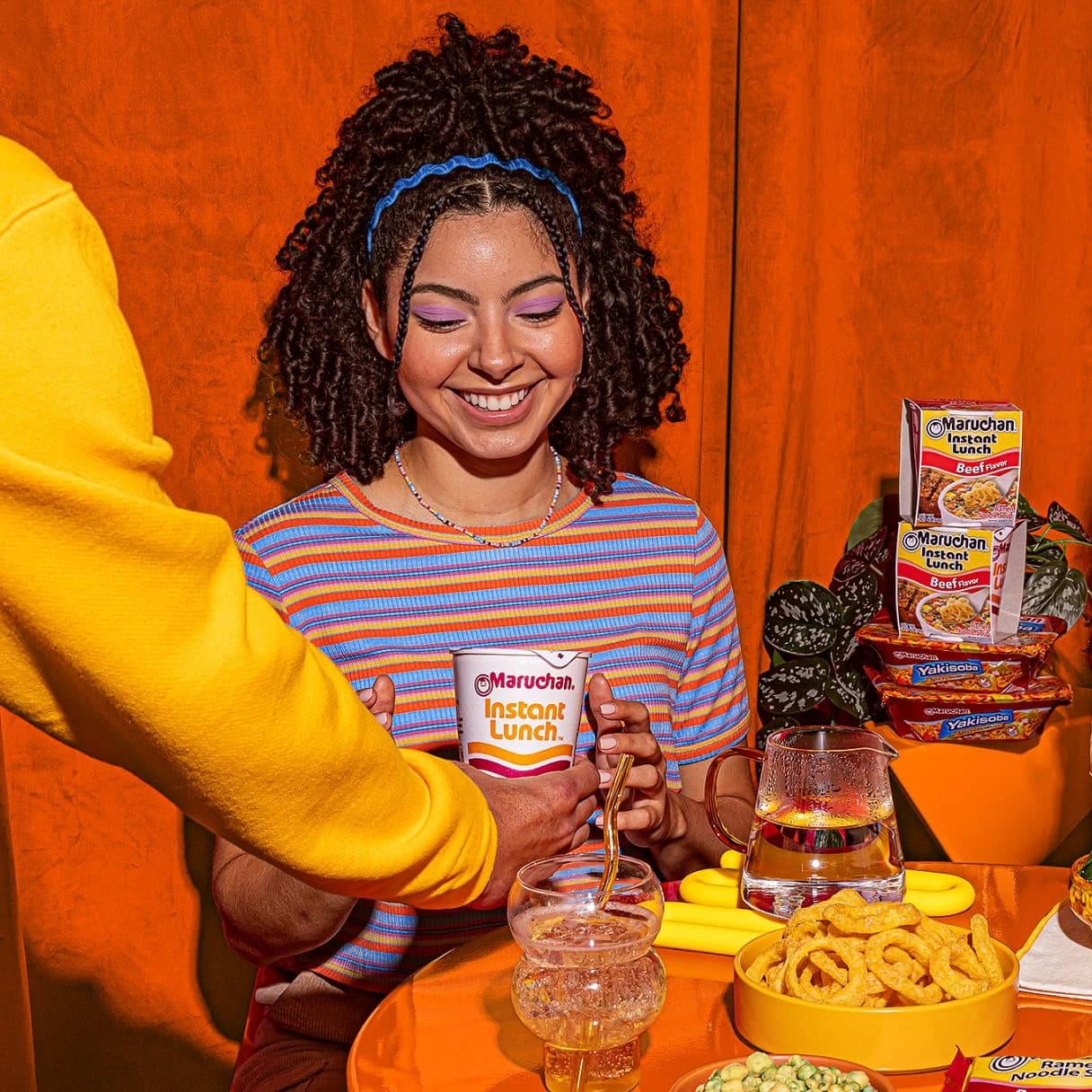 Woman smiling while holding an instant ramen cup at a dinner table