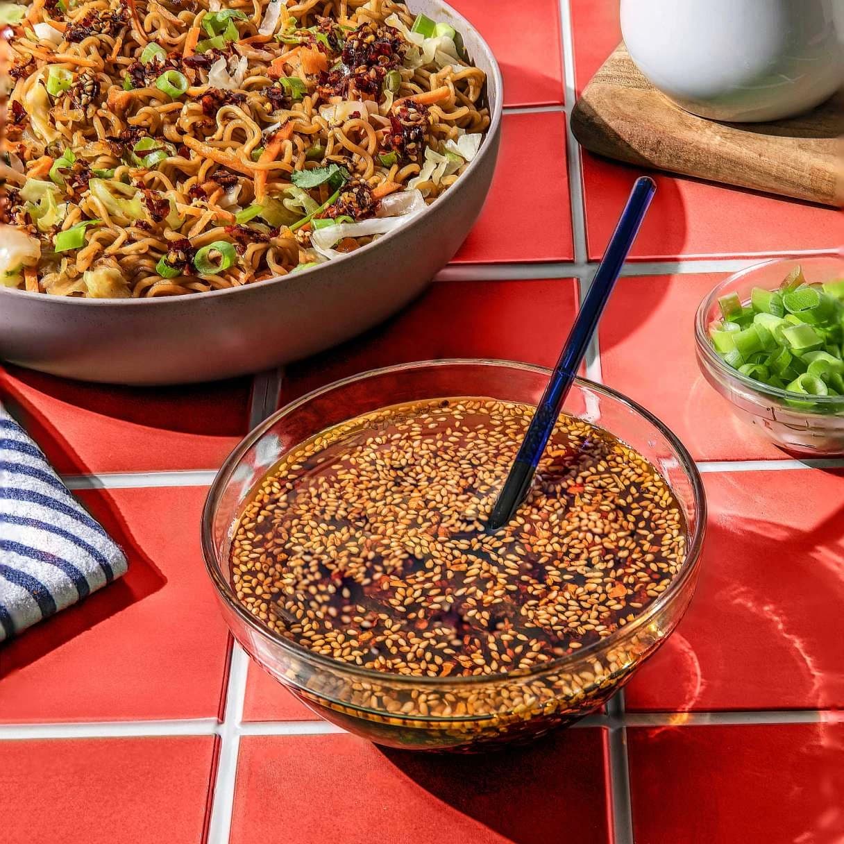 Bowl of teriyaki beef flavor yakisoba on a table next to a bowl of sauce